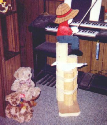 photo of a wooden boy perched atop a set of logs, with a fishing pole