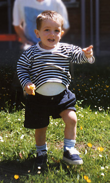 Happy 18 month old boy with big tummy is pointing on grass with buttercups and daisies